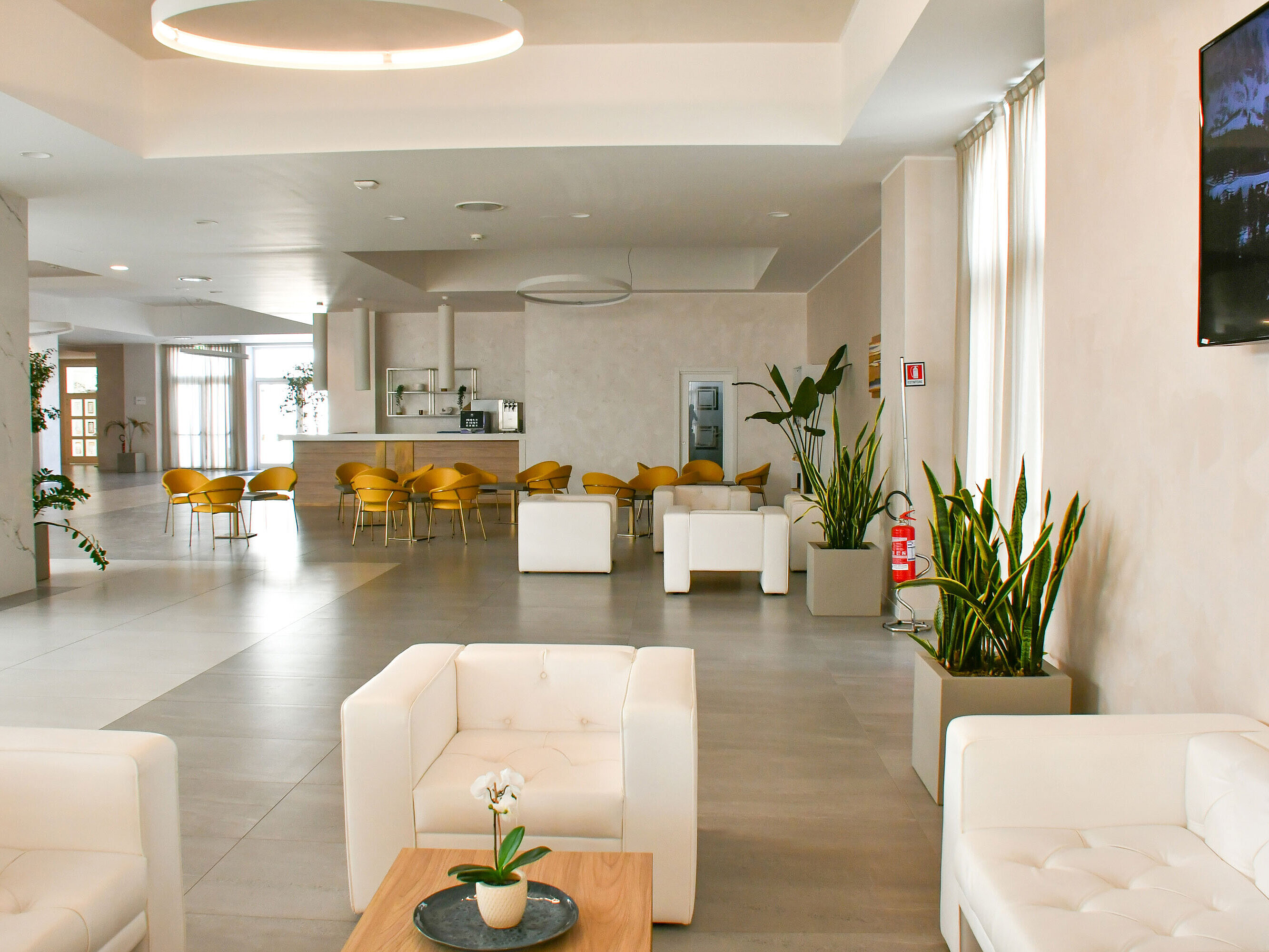 Lichtdurchflutete Lobby des Maritim Resort Calabria mit weißen Sesseln und gelben Stühlen
