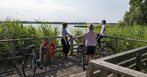 Fahrradtour Drei Frauen machen eine Pause auf einer Fahrradtour an einem Steg mit Blick auf den See beim Maritim Timmendorfer Strand.