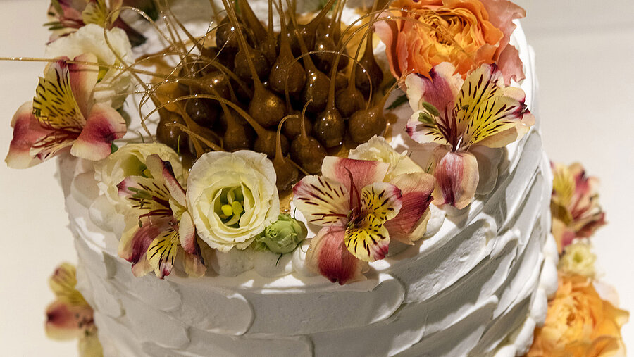 Hochzeitstorte mit eleganten Blumen und einer einzigartigen karamellisierten Dekoration auf der Spitze.