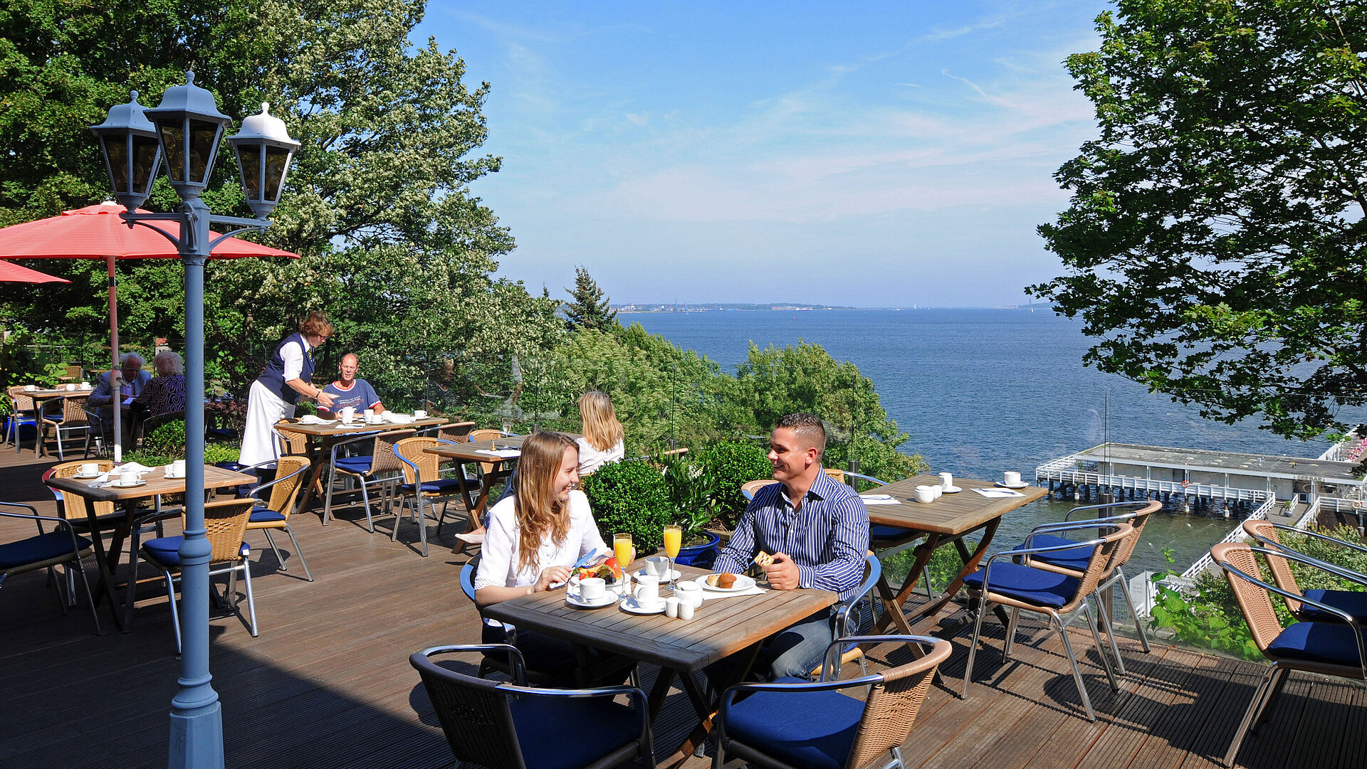 Panorama Terrasse Panorama Terrasse im Maritim Hotel Kiel mit Gästen beim Frühstück, sonniges Wetter und Blick auf die Förde im Hintergrund.