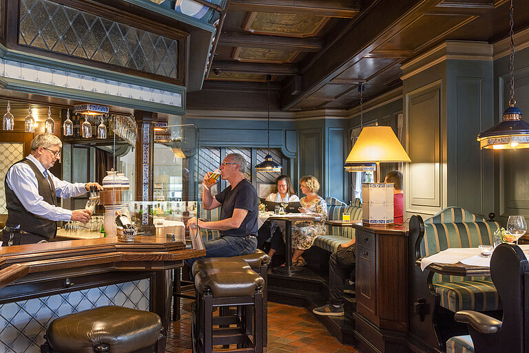 Gemütliche Hotelbar im traditionellen Stil mit Gästen, die Getränke genießen, und einem Barkeeper, der Bier zapft.