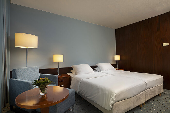 Classic Zimmer im Maritim Hotel Darmstadt mit einem Doppelbett, einem Sessel und dezenten Lampen.