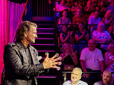 Entertainer bei einer Live-Show vor Publikum in stimmungsvoll beleuchtetem Veranstaltungsraum.