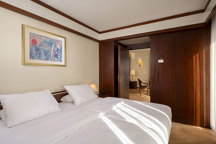Helles Schlafzimmer mit Doppelbett und Kunstwerk an der Wand in der Senior Suite des Maritim Hotels Köln.