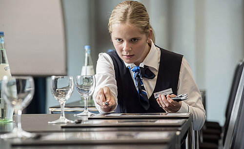 Servicekraft richtet den Tagungsraum im Maritim Hotel Bad Homburg mit Gläsern und Schreibmaterial her.