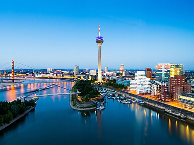 Düsseldorf Skyline mit Rheinturm, Rheinpromenade und moderner Architektur bei Abenddämmerung.