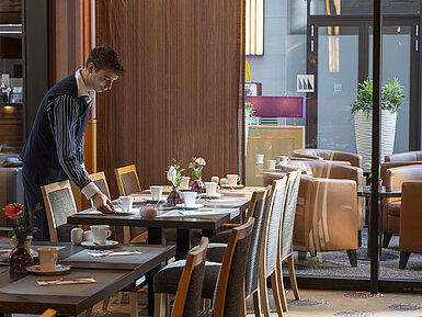 Mitarbeiter deckt einen Tisch im Restaurant Classico des Maritim Hotel Düsseldorf, umgeben von eleganter Einrichtung.