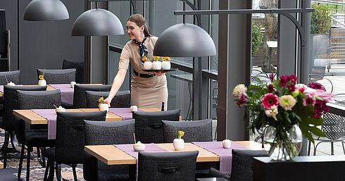 Servicekraft im Restaurant Wintergarten im Maritim Hotel Dresden bereitet stilvoll gedeckte Tische vor.