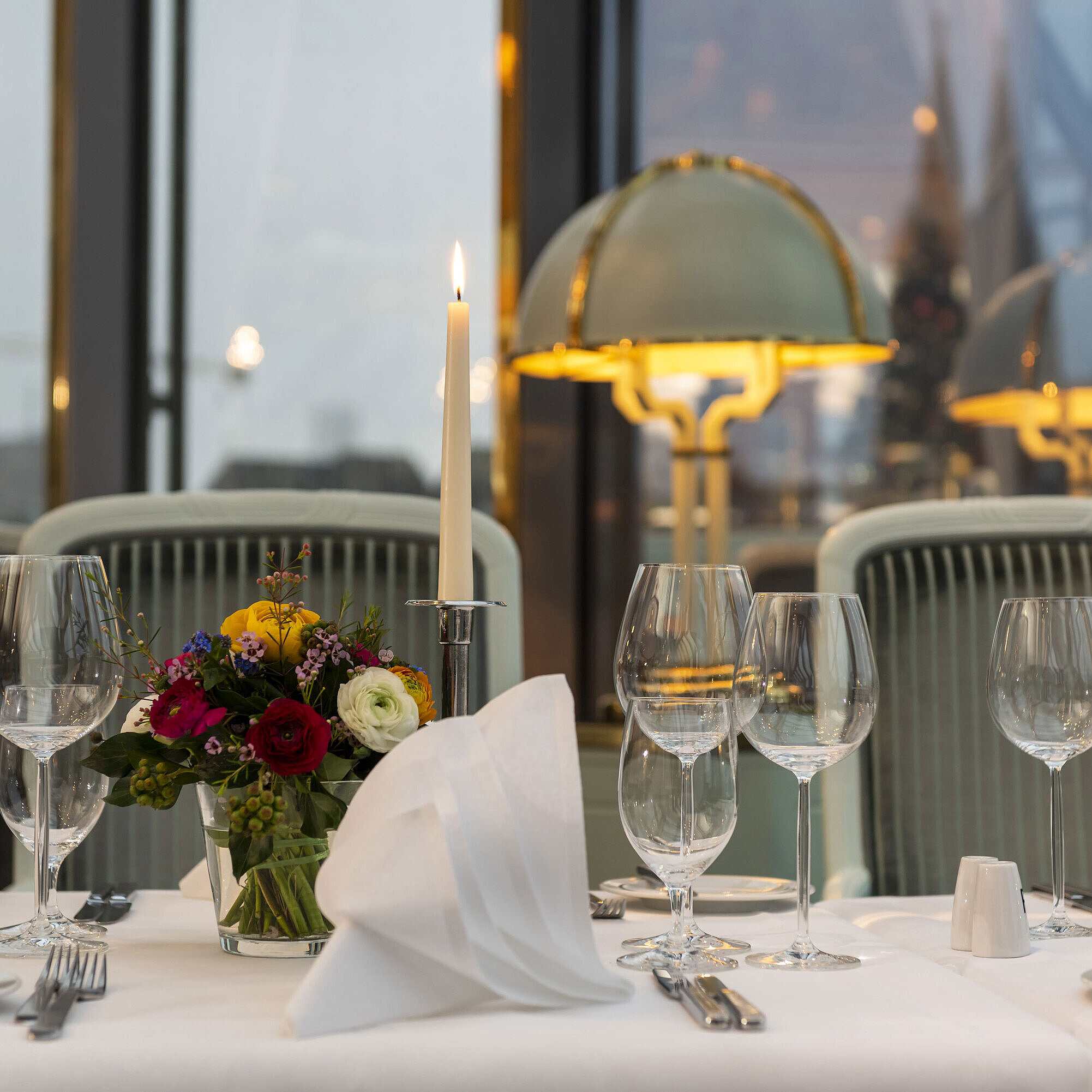 Elegant gedeckter Tisch im Restaurant mit Kerze, Weingläsern und Blumenarrangement, perfekt für ein gehobenes Abendessen.