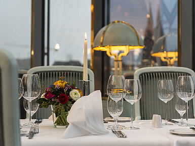 Elegant gedeckter Tisch im Restaurant mit Kerze, Weingläsern und Blumenarrangement, perfekt für ein gehobenes Abendessen.