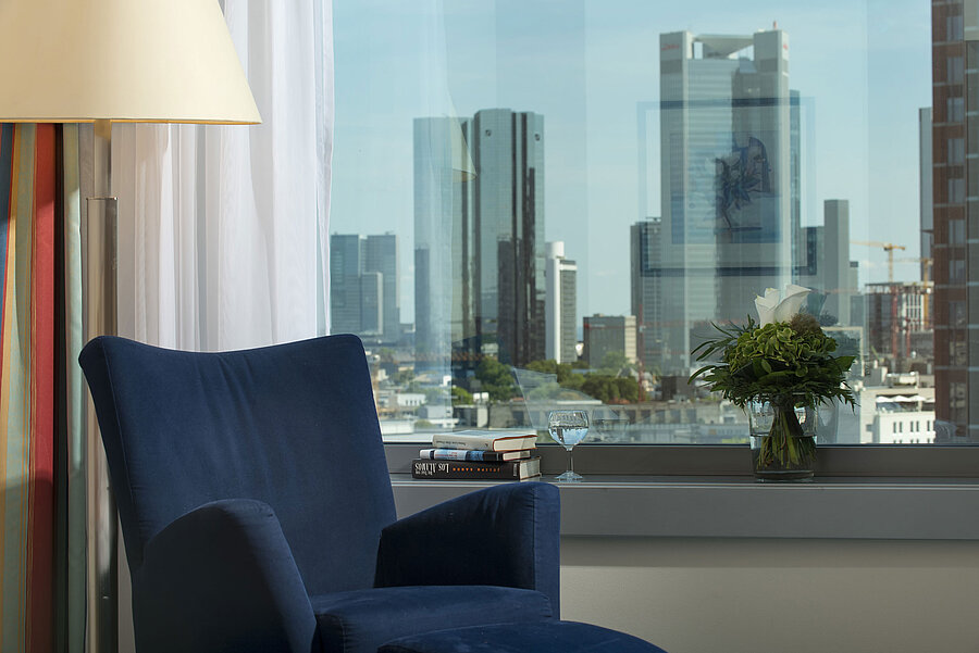 Ausblick aus einer Suite im Maritim Hotel Frankfurt mit Skyline-Blick, blauem Sessel und dekorativem Blumenarrangement.