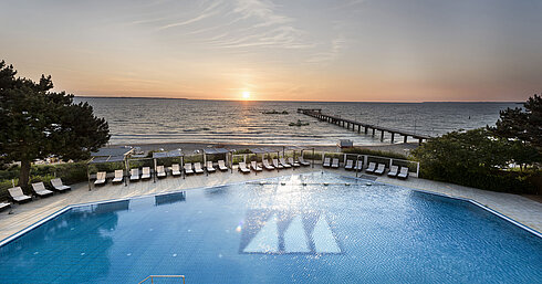 Pool mit Meerblick im Maritim Seehotel Timmendorfer Strand bei Sonnenuntergang, Liegen und Steg am Strand.