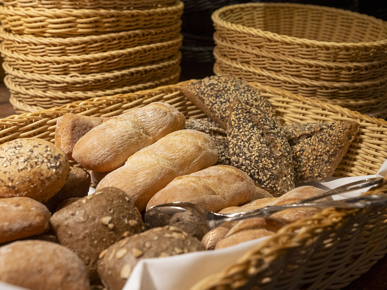 Verschiedene frische Brötchen mit Körnern und Saaten in Körben am Frühstücksbuffet.