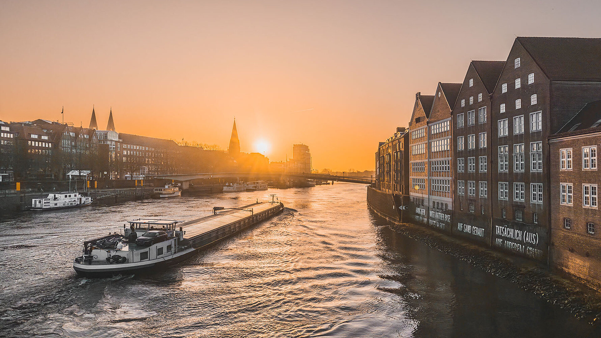 Bremen an der Weser bei Sonnenuntergang mit historischen Gebäuden am Ufer und Schiffen auf dem Fluss
