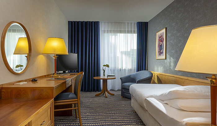 Freundlich eingerichtetes Zimmer mit Schreibtisch, Bett und Sessel im Maritim Hotel Magdeburg