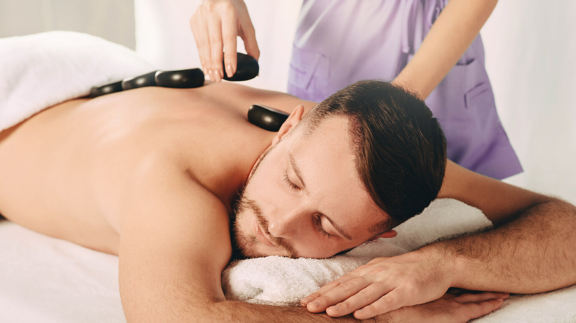 © Peakstock - AdobeStock.com Mann genießt wohltuende Hot-Stone-Massage im Spa für tiefe Entspannung