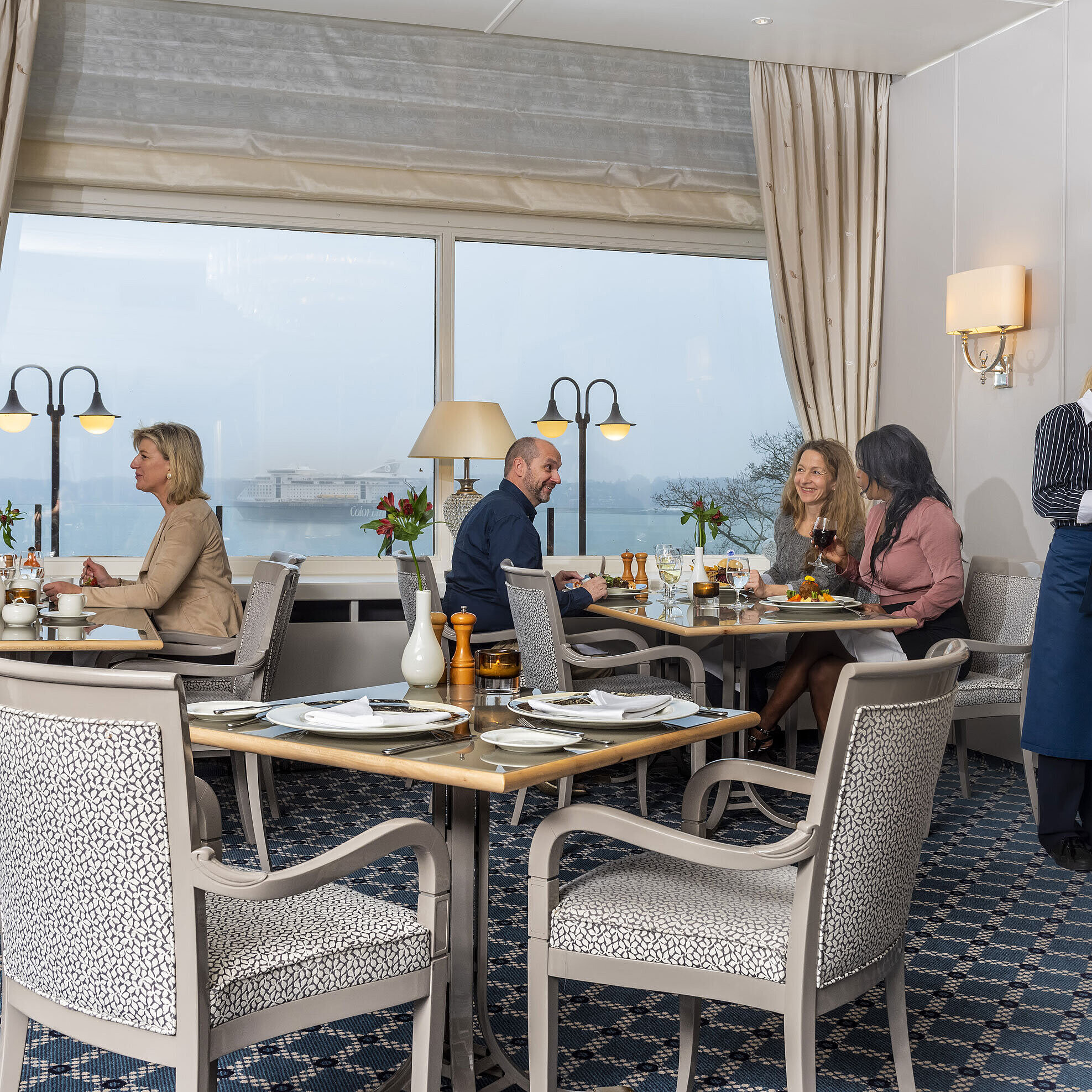 Das Restaurant Bellevue im Maritim Hotel Kiel, Gäste genießen Mahlzeiten mit Meerblick, freundlicher Service in stilvoller Umgebung.