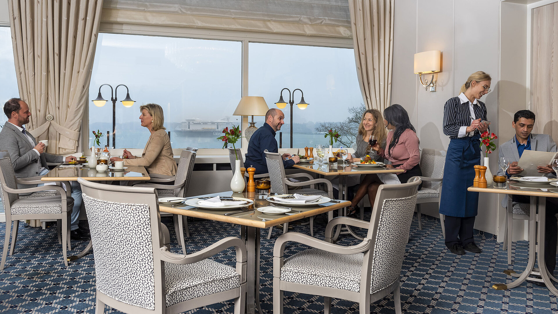 Das Restaurant Bellevue im Maritim Hotel Kiel, Gäste genießen Mahlzeiten mit Meerblick, freundlicher Service in stilvoller Umgebung.