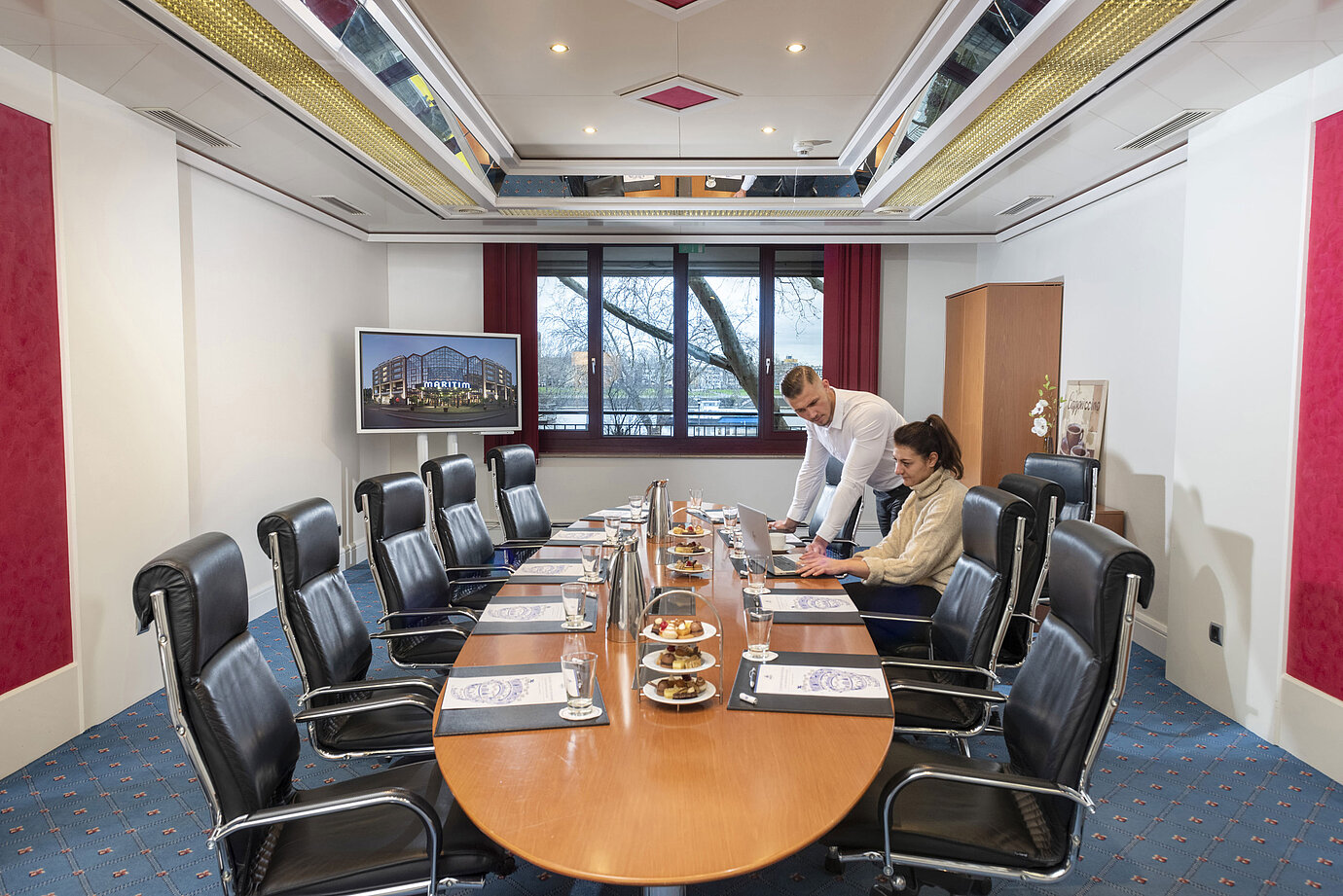 Zwei Personen arbeiten im Salon Boardroom des Maritim Köln mit Laptops an einem Besprechungstisch mit Getränken und Snacks.