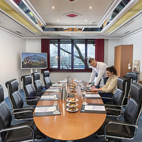 Zwei Personen arbeiten im Salon Boardroom des Maritim Köln mit Laptops an einem Besprechungstisch mit Getränken und Snacks.