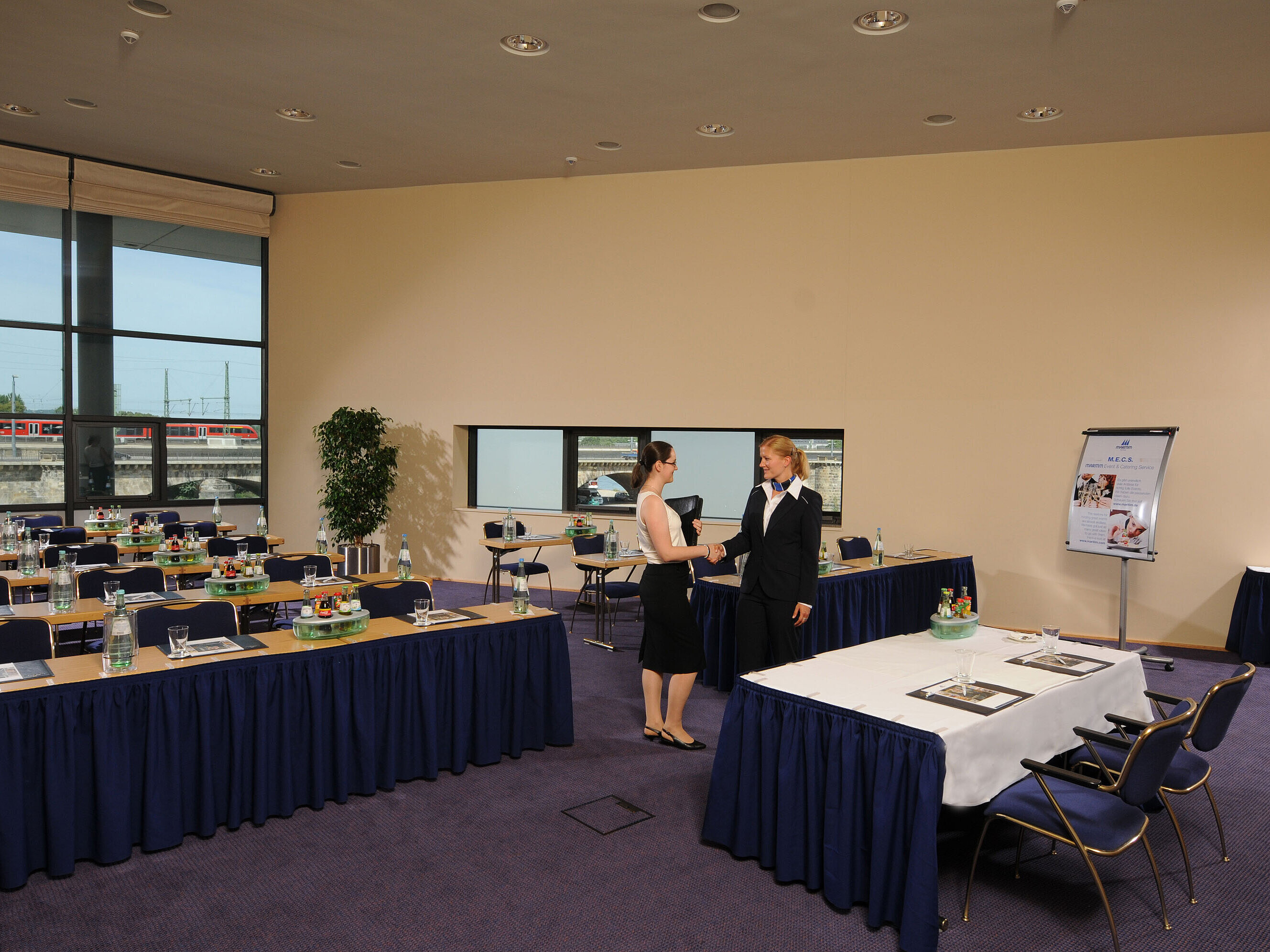 Heller Tagungsraum im Maritim Hotel Dresden mit gedeckten Tischen, Flipchart und zwei Personen beim Händeschütteln.