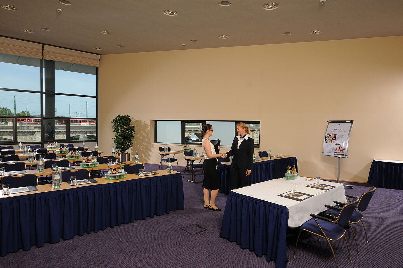 Heller Tagungsraum im Maritim Hotel Dresden mit gedeckten Tischen, Flipchart und zwei Personen beim Händeschütteln.