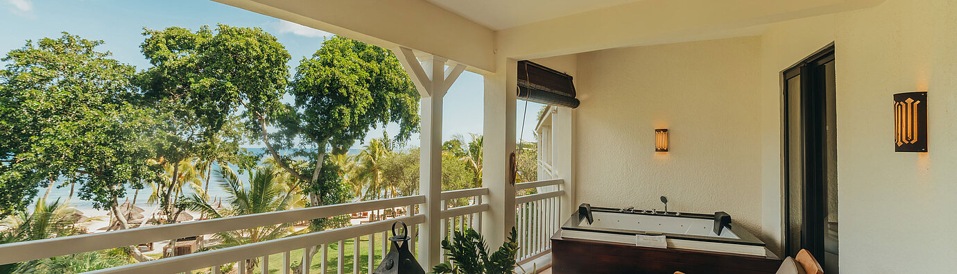 Terrasse der Penthouse Suite mit Sitzmöbeln, Liegen und Blick auf tropische Vegetation und Meer.