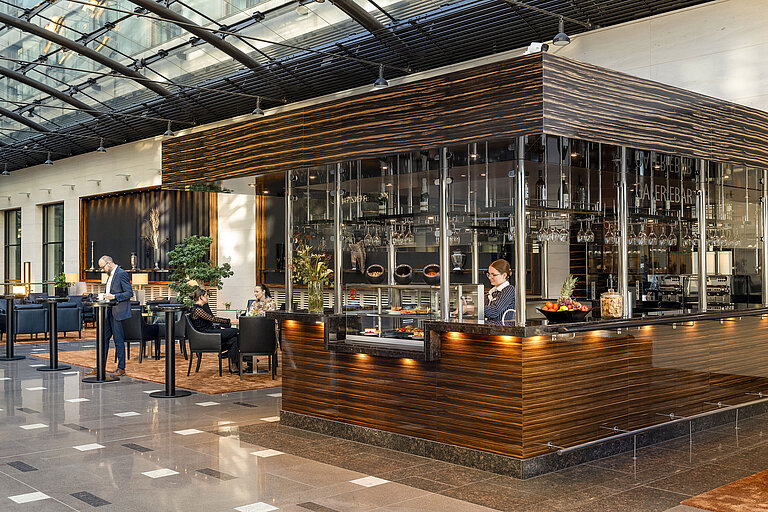 Moderne Bar im Maritim Hotel Düsseldorf mit eleganter Ausstattung, Sitzbereichen und einer Mitarbeiterin hinter der Theke.
