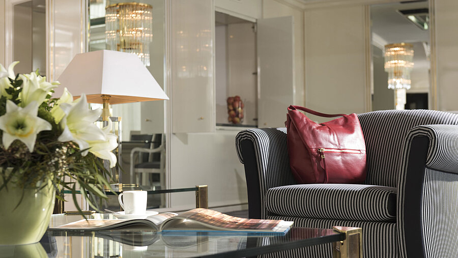 Detail in der Suite des Maritim Hotel Ulm mit gestreiftem Sessel, roter Handtasche und Lilienstrauß