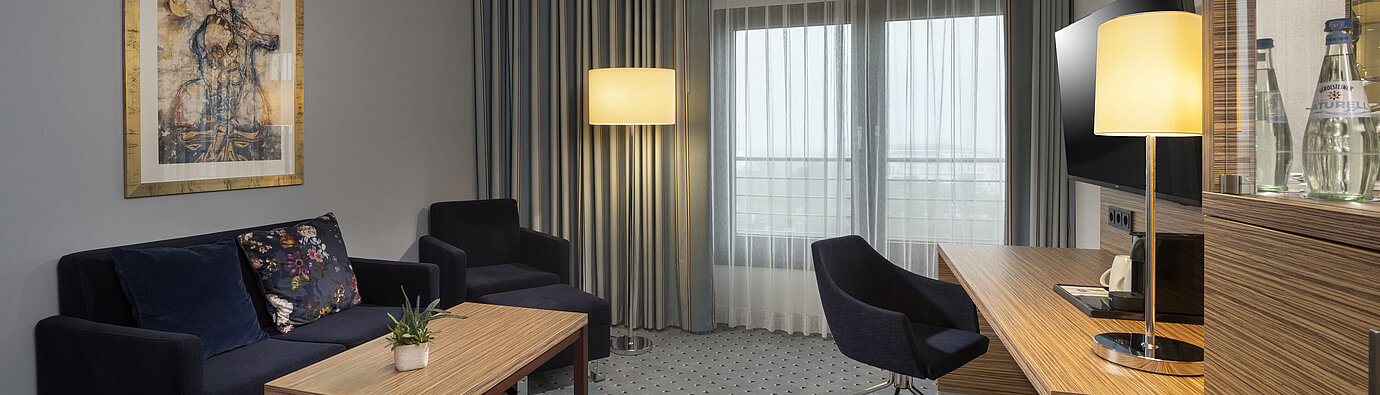 Junior Suite mit stilvoller Einrichtung, Sofa, Schreibtisch, Fernseher und großen Fenstern für viel Tageslicht.