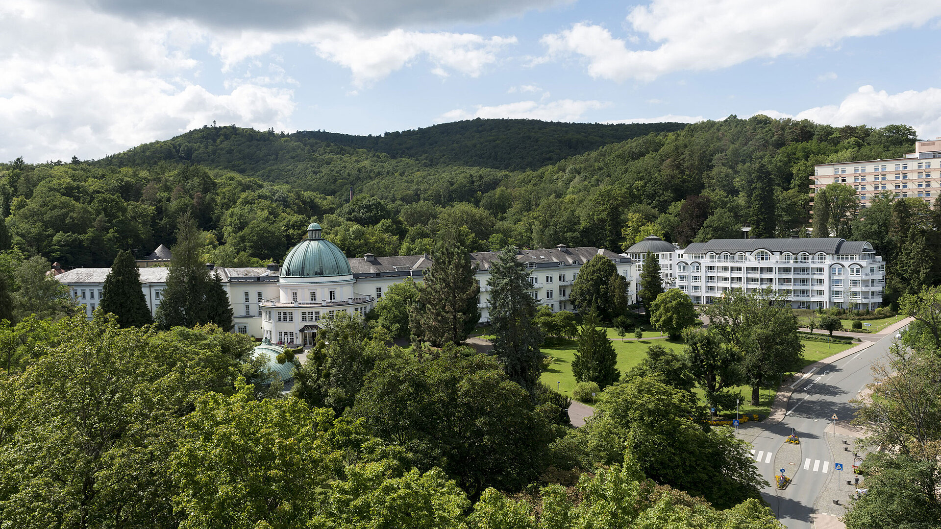 Blick auf das Maritim Hotel Bad Wildungen, umgeben von Bäumen und der grünen Landschaft des Kurparks.