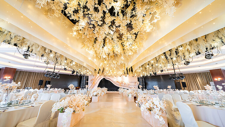 Prächtig dekorierter Hochzeitssaal mit floraler Deckeninstallation, elegantem Bühnenbereich und stilvoller Bestuhlung