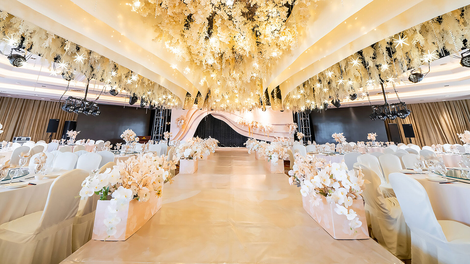 Prächtig dekorierter Hochzeitssaal mit floraler Deckeninstallation, elegantem Bühnenbereich und stilvoller Bestuhlung