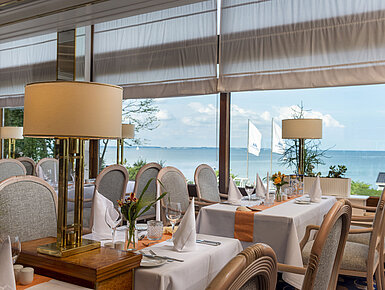 Elegantes Restaurant mit gedeckten Tischen und Meerblick, dekoriert mit Lampen und Blumen für ein gehobenes Speiseerlebnis.