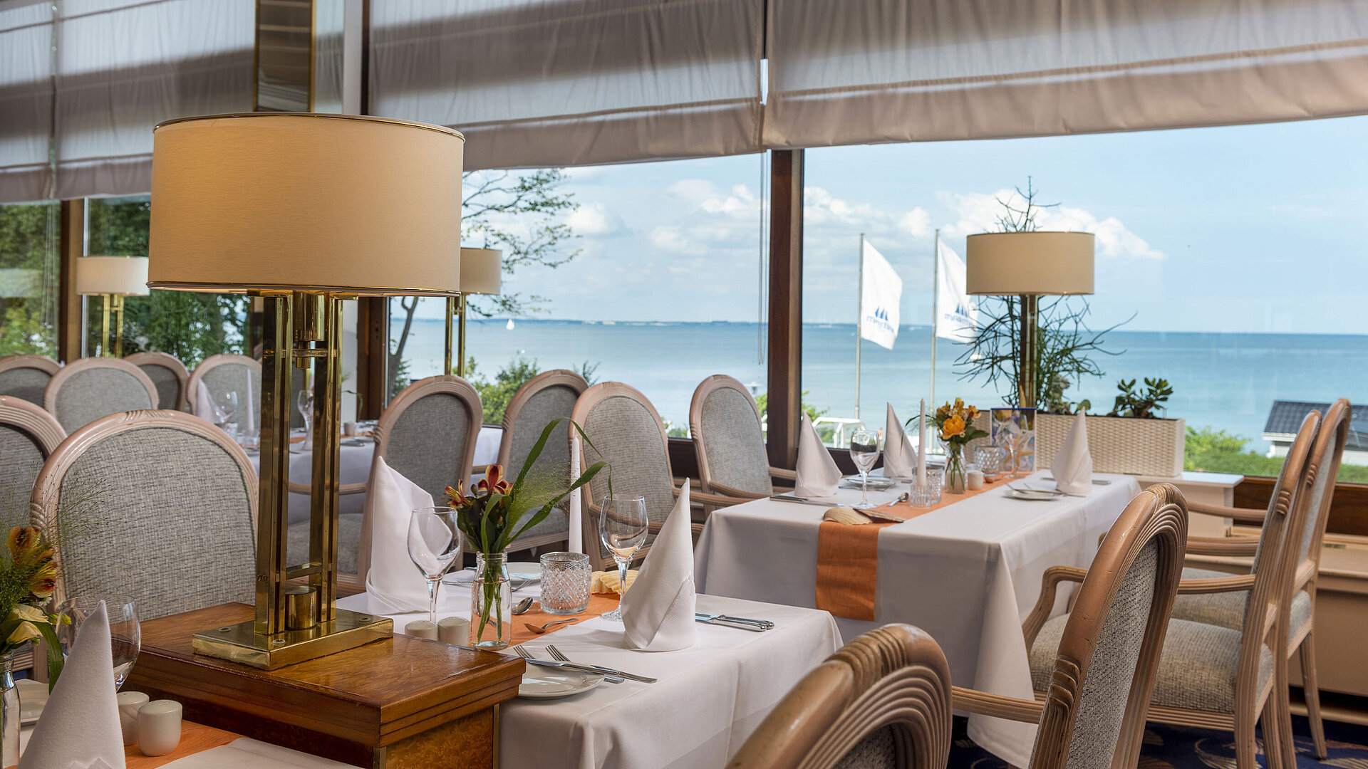 Elegantes Restaurant mit gedeckten Tischen und Meerblick, dekoriert mit Lampen und Blumen für ein gehobenes Speiseerlebnis.