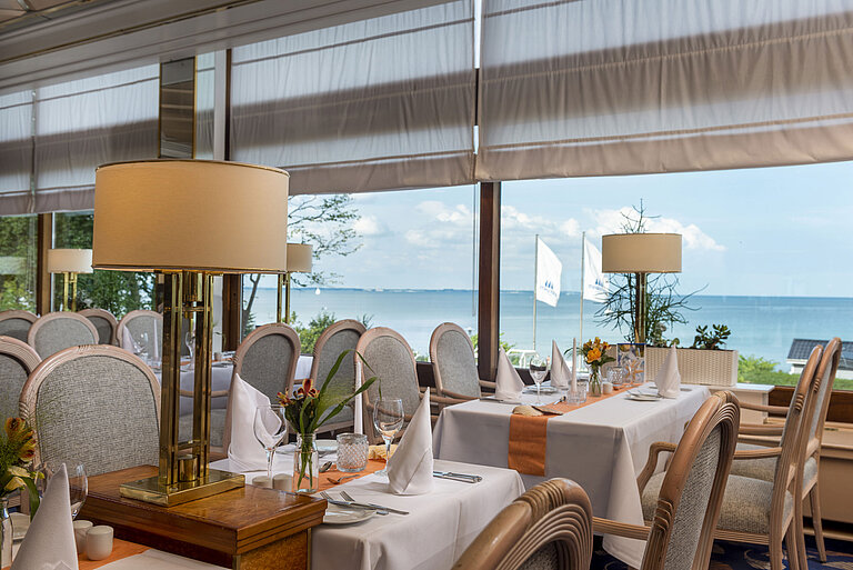 Elegantes Restaurant mit gedeckten Tischen und Meerblick, dekoriert mit Lampen und Blumen für ein gehobenes Speiseerlebnis.