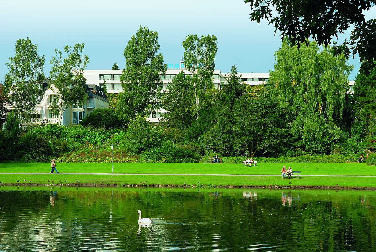 Außenansicht Blick auf das Maritim Hotel Bad Salzuflen hinter dem grünen Kurpark mit See und Schwan