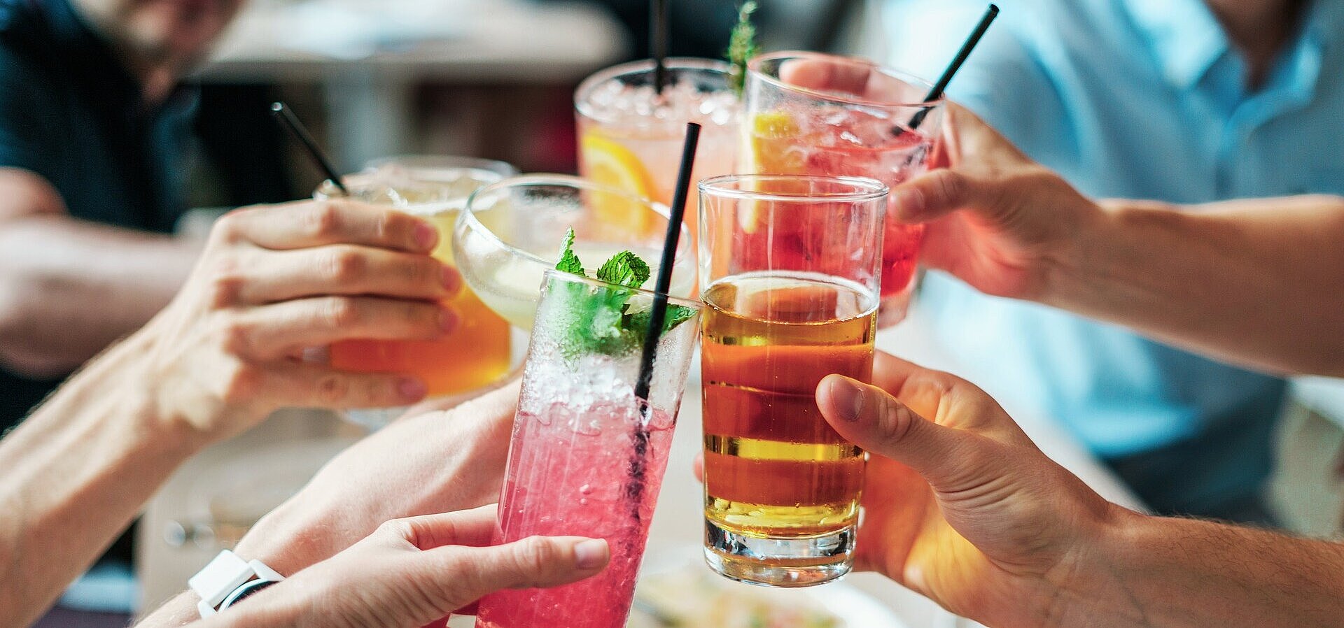Gemeinsamer Anstoß mit Getränken Mehrere Personen stoßen mit bunten Getränken und Cocktails in Gläsern bei geselligem Beisammensein an.