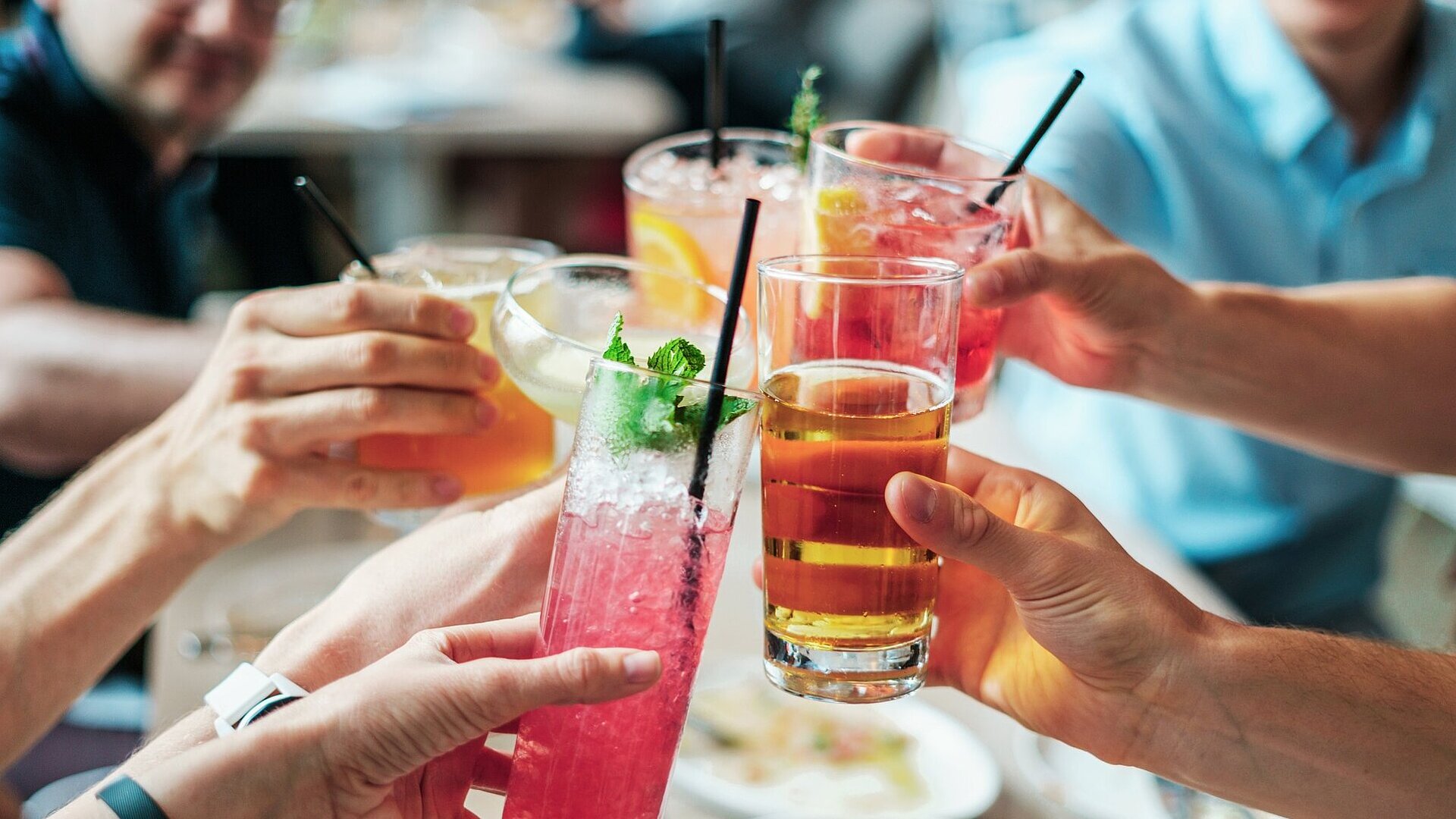 Mehrere Personen stoßen mit bunten Getränken und Cocktails in Gläsern bei geselligem Beisammensein an.