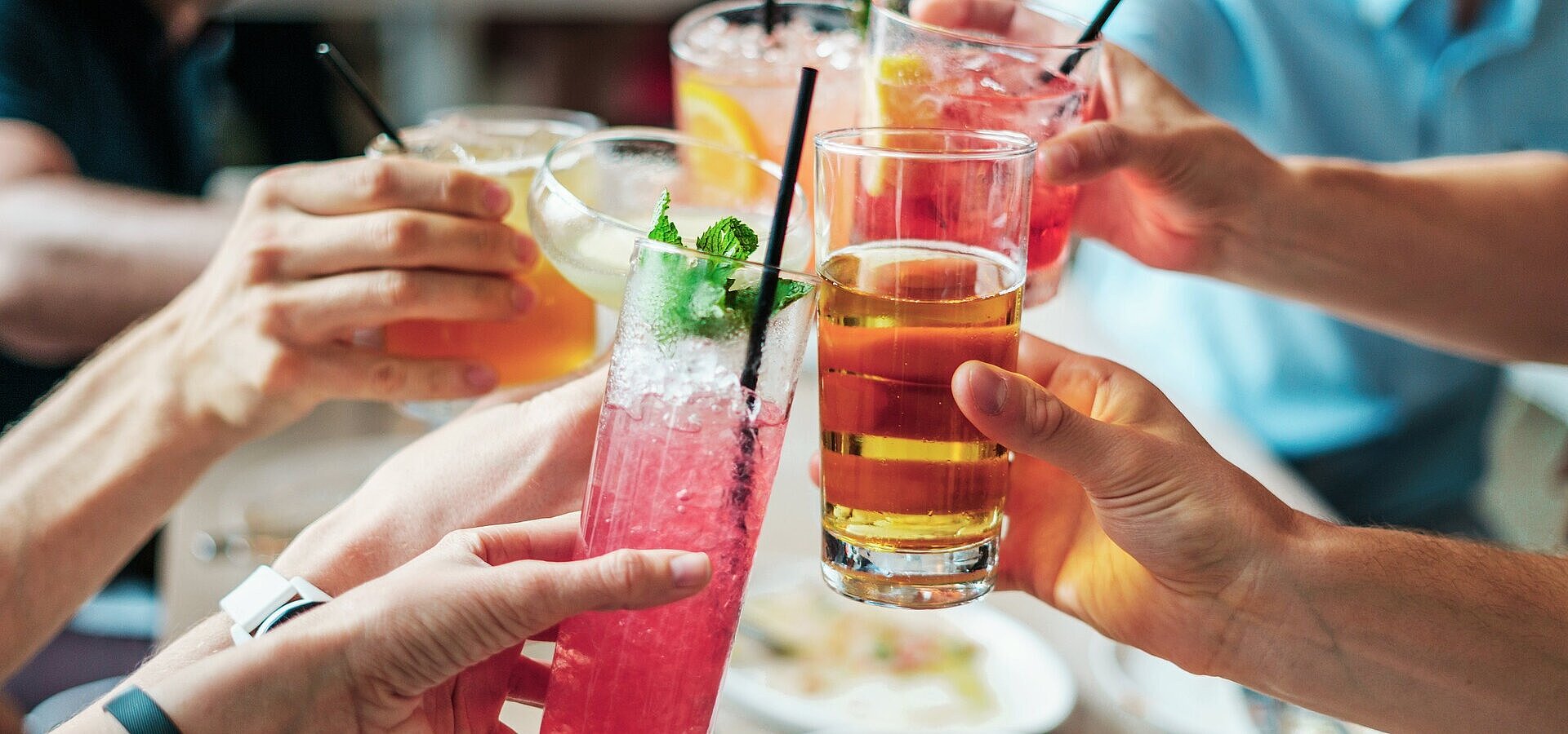 Gemeinsamer Anstoß mit Getränken Mehrere Personen stoßen mit bunten Getränken und Cocktails in Gläsern bei geselligem Beisammensein an.