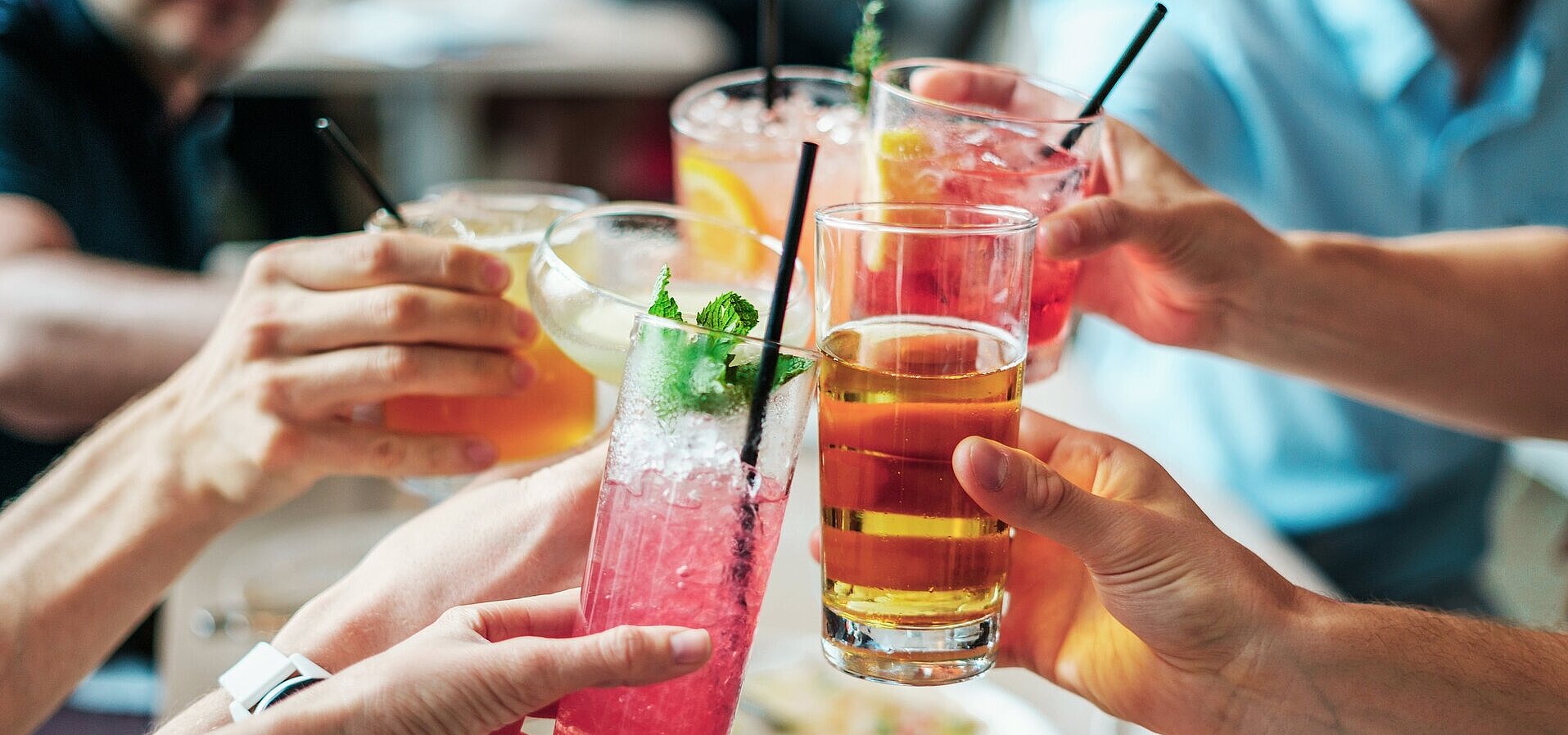 Mehrere Personen stoßen mit bunten Getränken und Cocktails in Gläsern bei geselligem Beisammensein an.