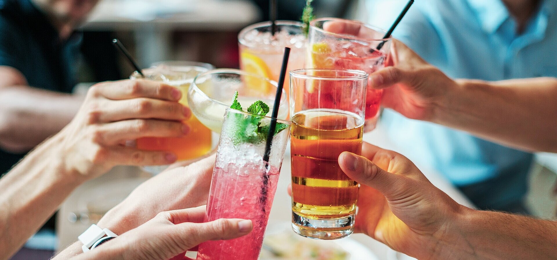 Gemeinsamer Anstoß mit Getränken Mehrere Personen stoßen mit bunten Getränken und Cocktails in Gläsern bei geselligem Beisammensein an.