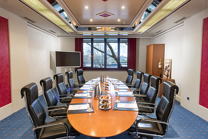 Der Salon Boardroom im Maritim Köln, eingerichtet mit einem ovalen Konferenztisch, Ledersesseln und Konferenzmaterialien.