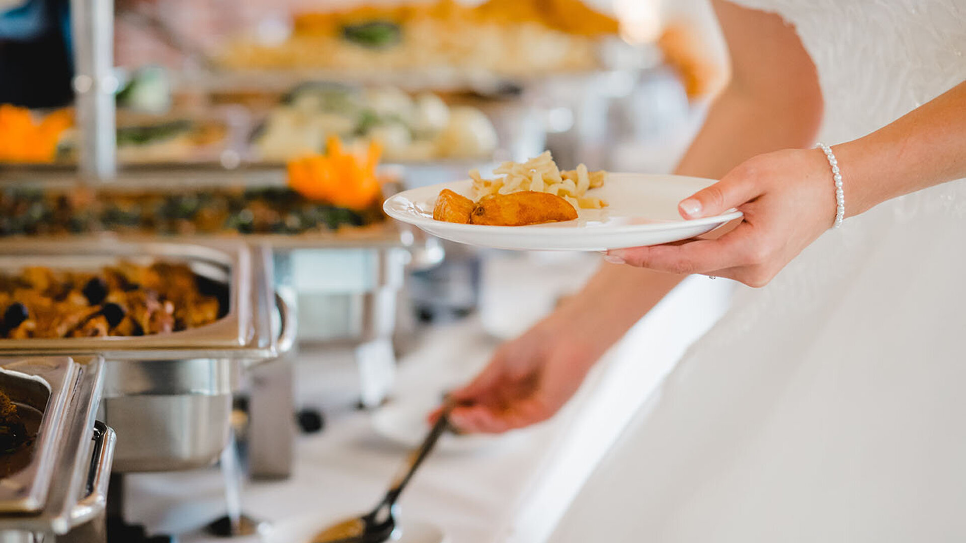© LElik83 - AdobeStock.com Gast bedient sich am warmen Buffet und füllt Speisen aus Edelstahlbehältern auf einen Teller