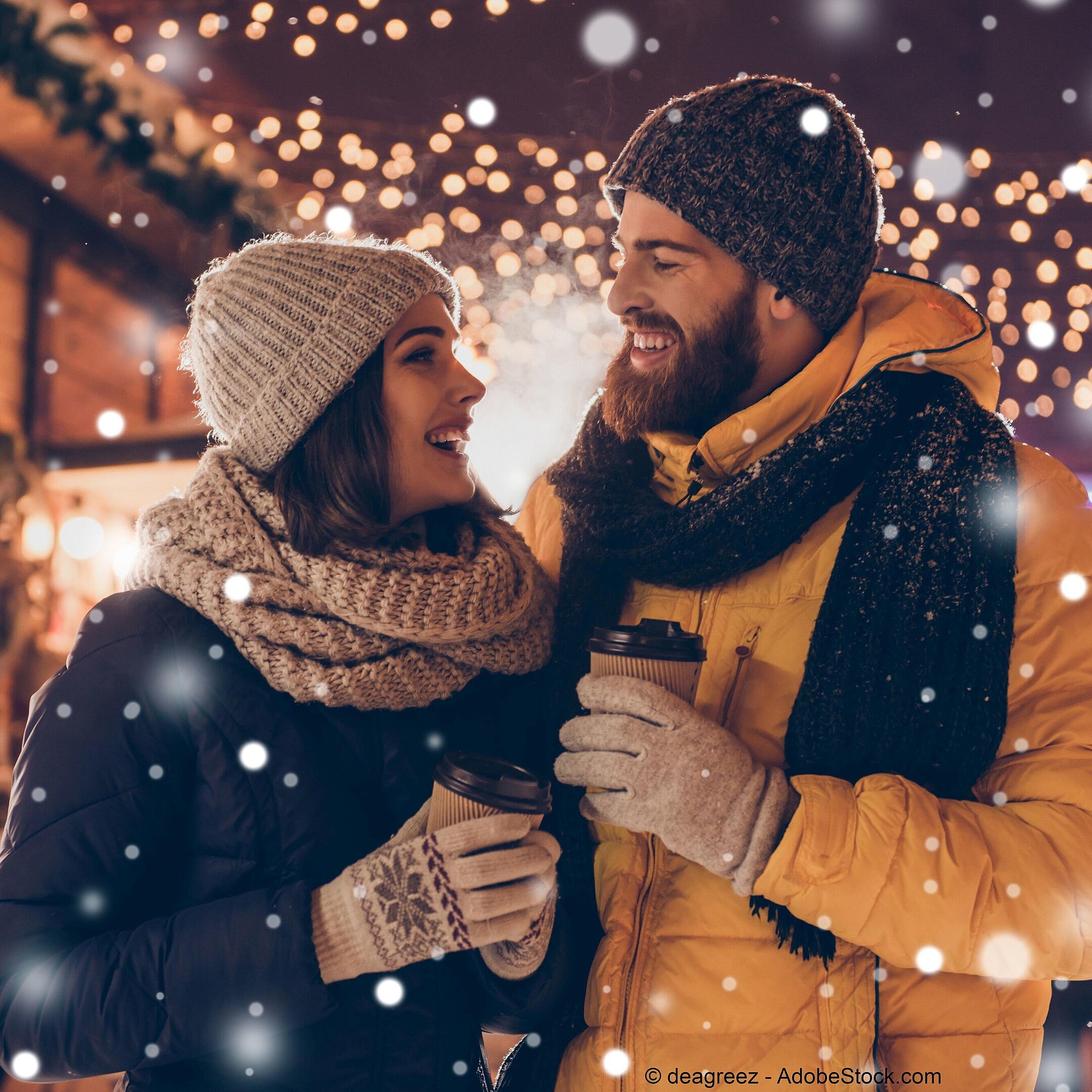 © deagreez - AdobeStock.com Paar genießt heiße Getränke auf einem winterlichen Weihnachtsmarkt