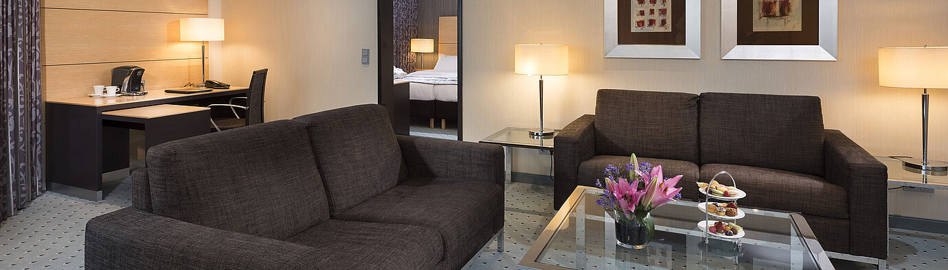Junior Suite im Maritim Hotel Düsseldorf mit separatem Wohnbereich, zwei Sofas, Schreibtisch, Blumen und modernem Design.