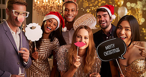 Elegante Gruppe bei festlicher Weihnachtsfeier mit Sekt und Weihnachtsmützen vor goldenem Hintergrund