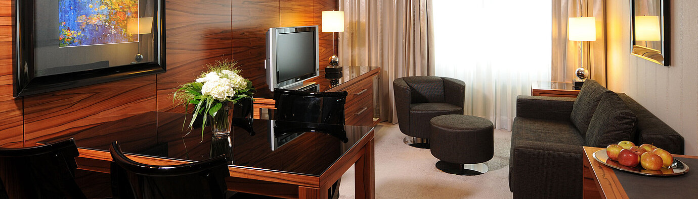 Heller Wohnbereich mit Sofa, Sessel, TV und Schreibtisch im Maritim Hotel München
