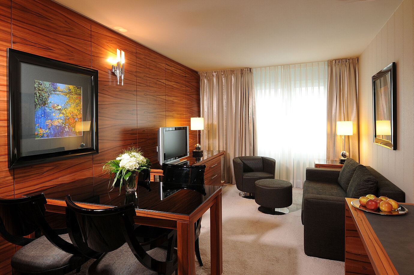 Heller Wohnbereich mit Sofa, Sessel, TV und Schreibtisch im Maritim Hotel München