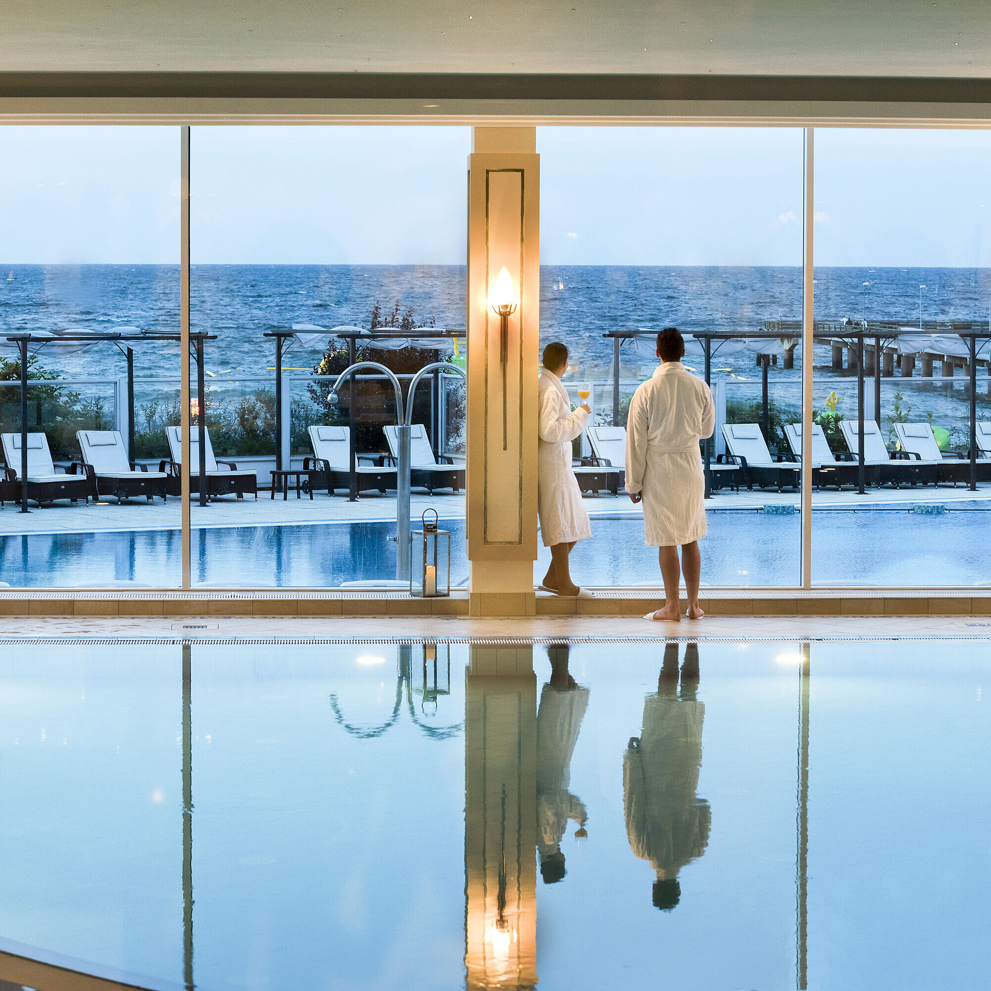 Innenpool mit Meerblick im Maritim Seehotel Timmendorfer Strand, zwei Gäste in Bademänteln am Fenster.
